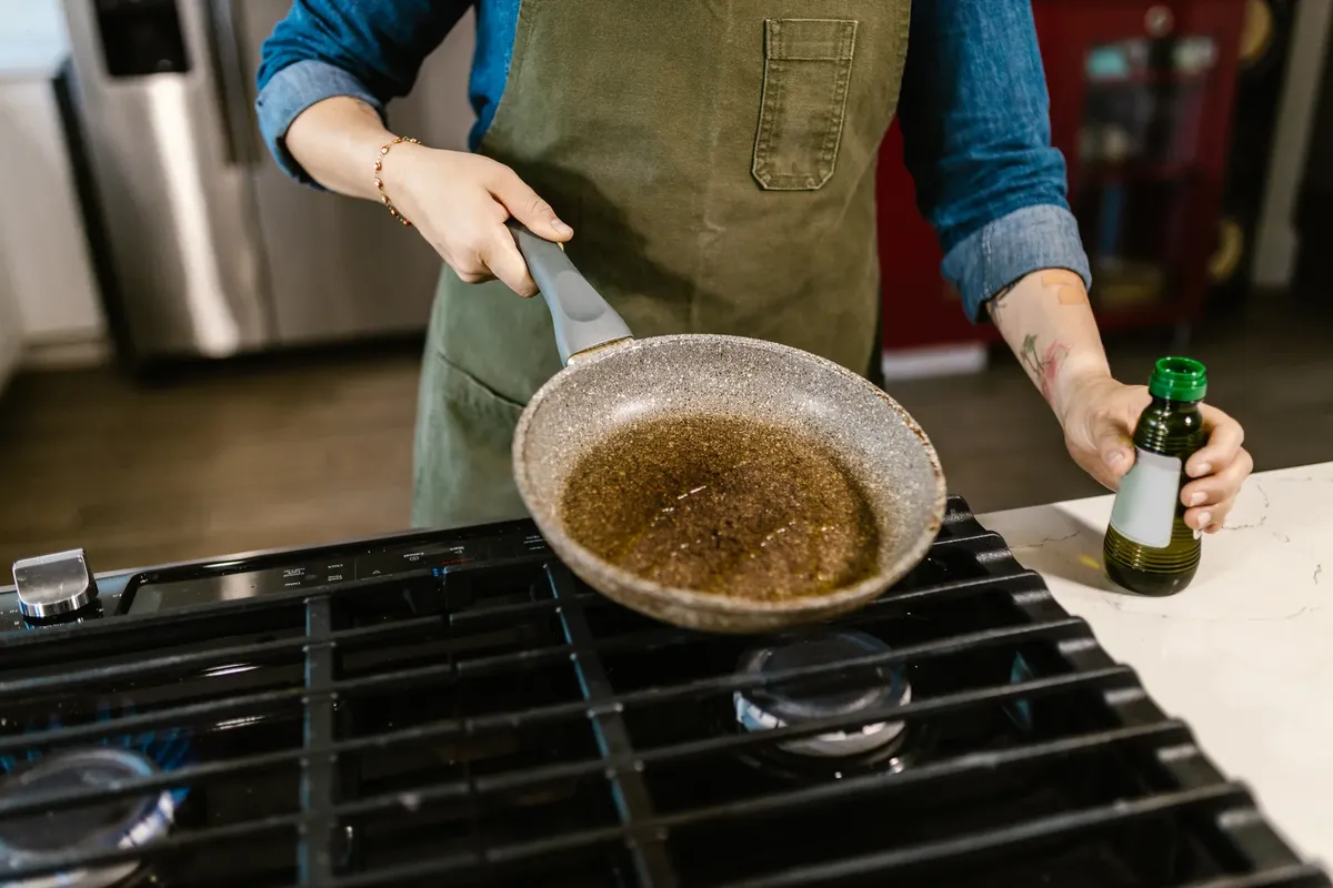 Chef holding frying pan with olive oil in kitchen, ready to cook a delicious meal.