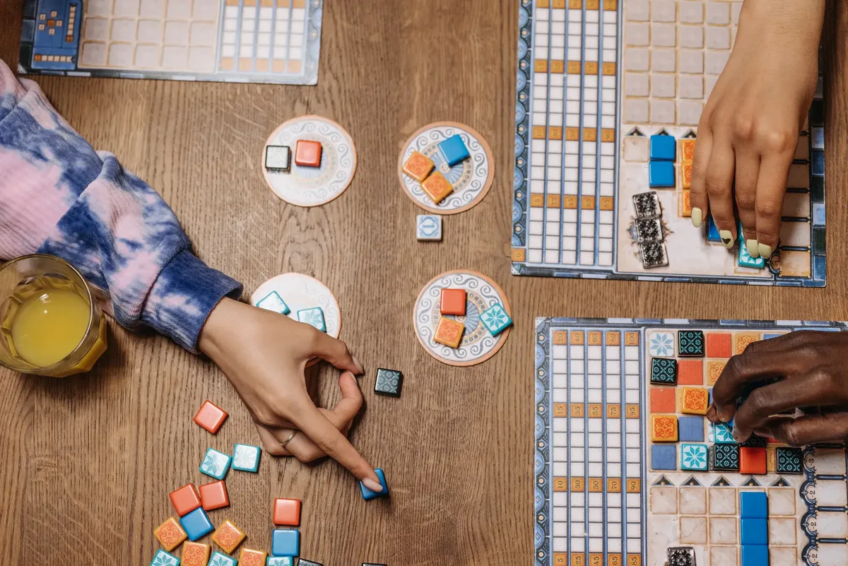 People enjoying a strategic board game on a wooden table with drinks, showcasing social interaction.