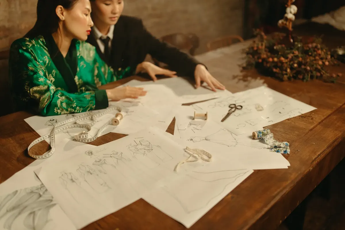 Two designers working on a fashion project with sketches and tools in a studio setting.